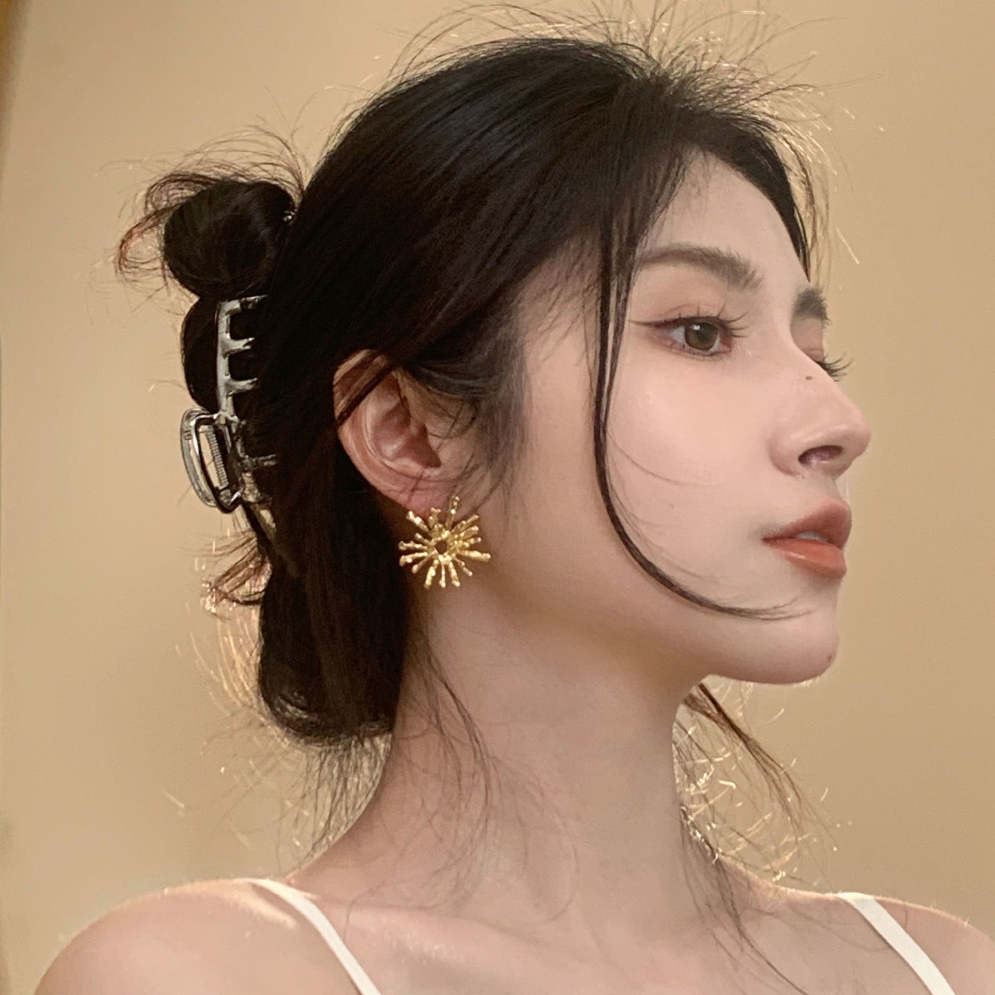 Woman wearing gold sun-shaped earrings with a neutral background