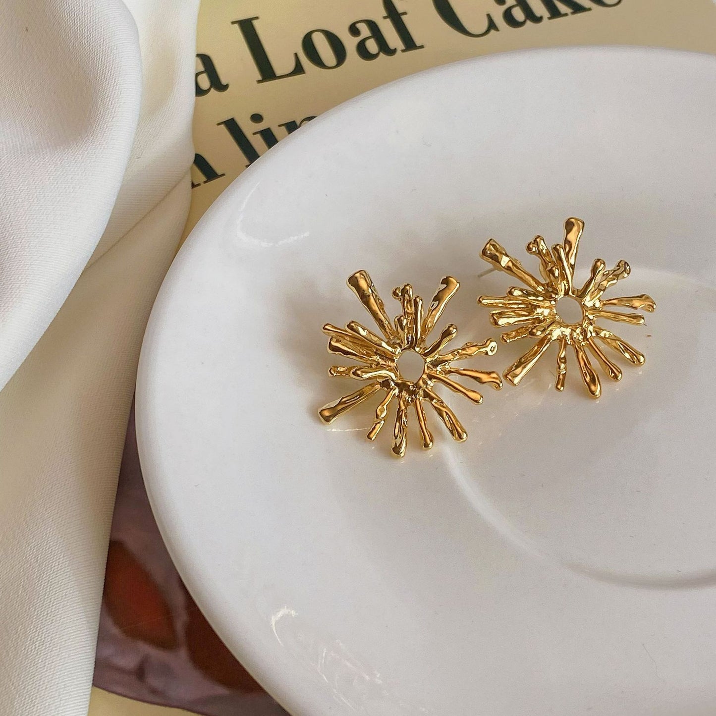 Gold sunburst earrings on a white dish with a magazine in the background