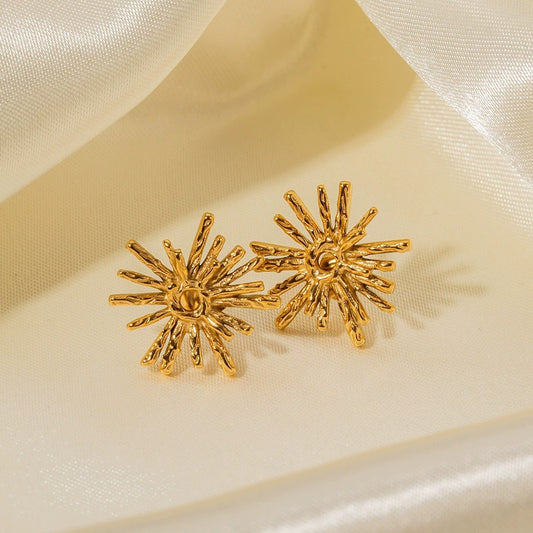 Gold sunburst earrings on a beige satin background